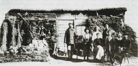 Une famille de colons devant sa cabane isolée avec des mottes de terre. Une famille de colons devant sa cabane isolée avec des mottes de terre.